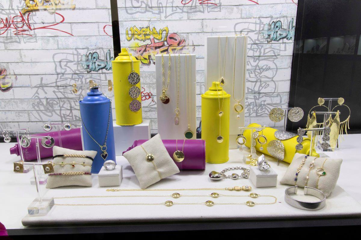 Assorted gold and silver jewelry—necklaces, bracelets, and earrings—on colorful display stands.
