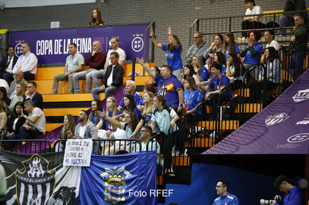 Spectators in orange seats at an indoor arena, many wearing blue, with banners reading Copa de la Reina in the background.