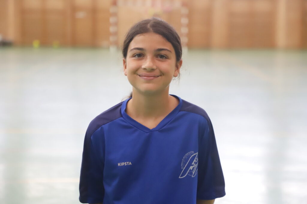 Smiling girl in a blue sports jersey standing in a gymnasium.