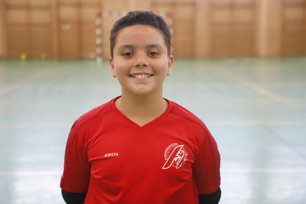 Niño sonriente con camiseta roja de fútbol sala en un pabellón