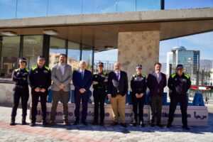 Group of uniformed police officers and suited officials standing in a row for a formal outdoor ceremony outside a modern building.