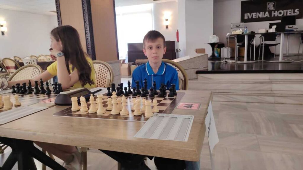 Niño sentado frente a un tablero de ajedrez en un torneo.
