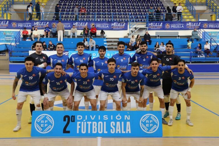 Futsal team in blue jerseys posing for a group photo on an indoor court, banner reads '2ª División Fútbol Sala' in front.