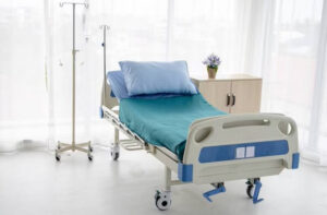 Cama de hospital con sábanas azules y almohadas en una habitación iluminada.