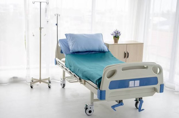Cama de hospital con sábanas azules y almohadas en una habitación iluminada.