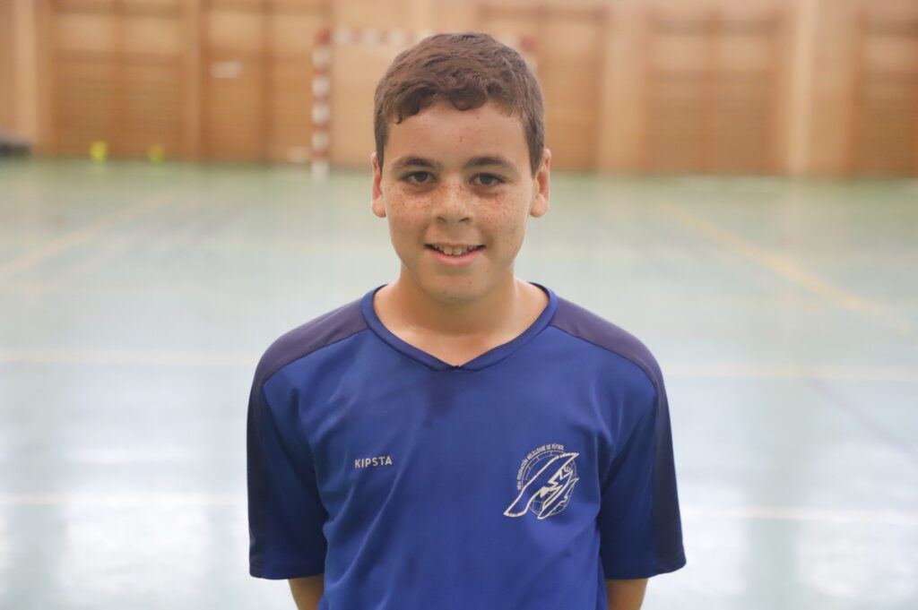 Smiling boy in a blue sports jersey standing in an indoor gymnasium