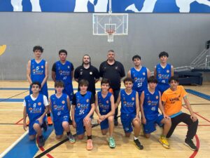 Group photo of a youth basketball team in blue uniforms with two coaches in black shirts standing behind them on a gym court.