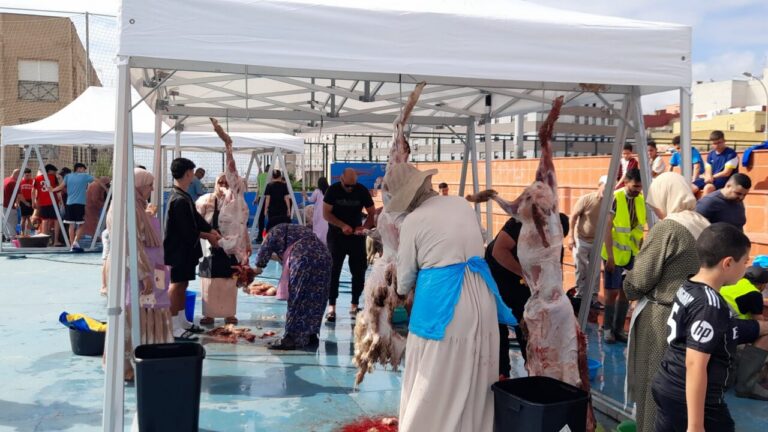 People under white canopies processing animal carcasses during a communal slaughter event; exposed meat, blood on the ground, and volunteers assisting.
