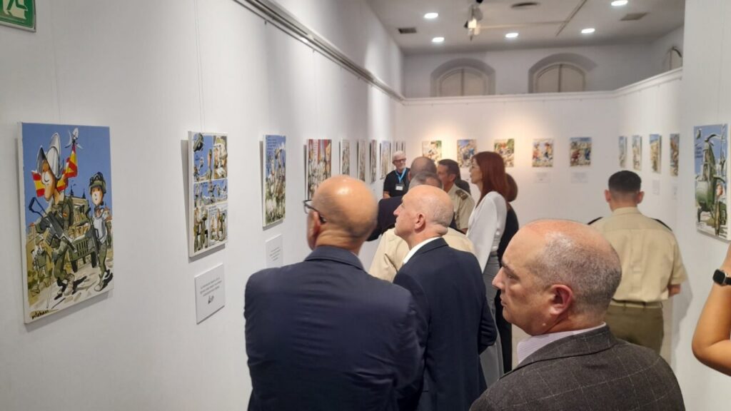 People in business attire watch colorful cartoon war-themed paintings displayed along white gallery walls at an art exhibition.
