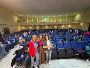 Tres mujeres posando en un auditorio lleno de niños sentados