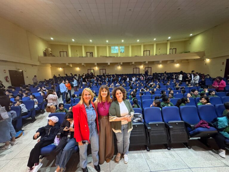 Tres mujeres posando en un auditorio lleno de niños sentados