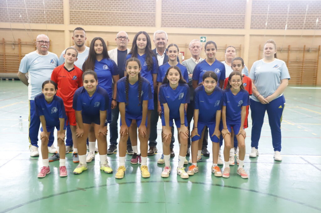 Girls' youth sports team posing with coaches in a gymnasium, all wearing blue uniforms and sneakers.