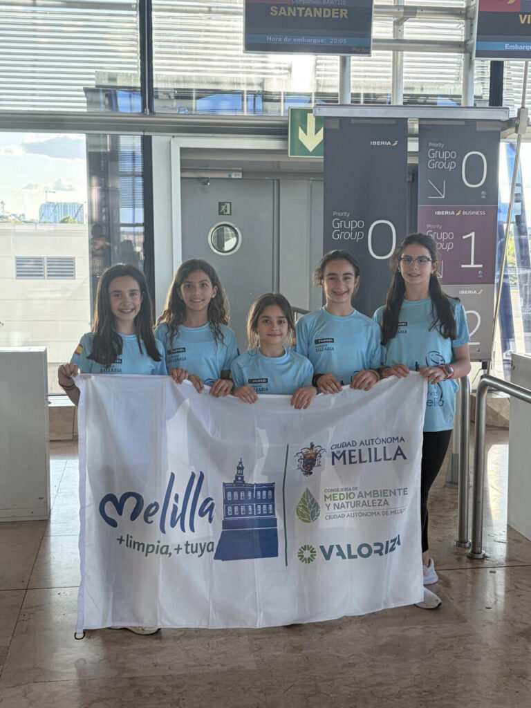 Gimnastas del Club Virka Melilla sosteniendo una bandera en el aeropuerto