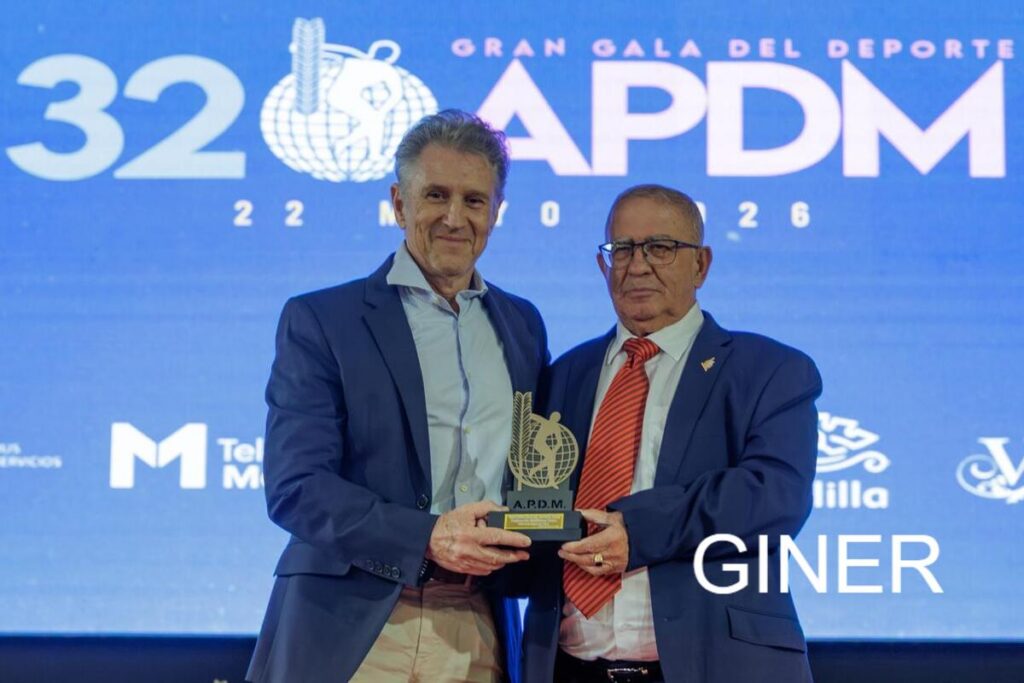 Two men in suits on stage holding a trophy at the 32 APDM Gran Gala del Deporte awards ceremony.