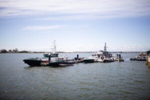 Boats docked at a marina on a calm river with a pier on the right and a clear blue sky above