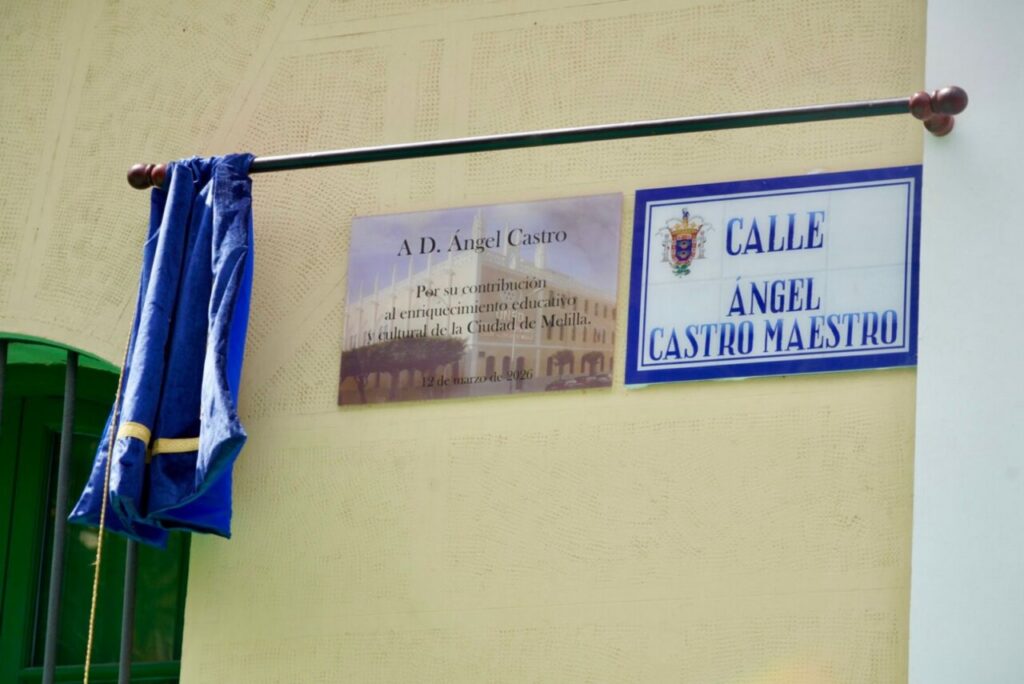 Blue curtain draped over a rod in front of a pale yellow wall, with a plaque and a street sign that read Calle Ángel Castro Maestro.