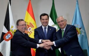 Three men in suits shake hands in the center, smiling, with multiple national flags in the background.