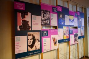 Row of colorful posters and timeline panels mounted on a wall, using magenta and blue tones with vintage photos and text details.