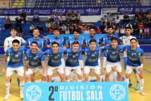 Group photo of a futsal team in blue jerseys posing on an indoor court, players kneeling in front and standing behind, with a banner reading '2ª División Fútbol Sala' in the foreground.