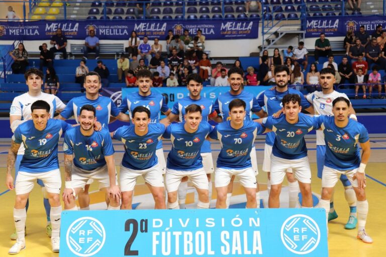 Group photo of a futsal team in blue jerseys posing on an indoor court, players kneeling in front and standing behind, with a banner reading '2ª División Fútbol Sala' in the foreground.