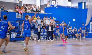 Basketball players in blue uniforms celebrating on court as crowd cheers from the stands behind them.