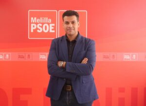 Hombre posando con brazos cruzados frente a un fondo rojo del PSOE en Melilla