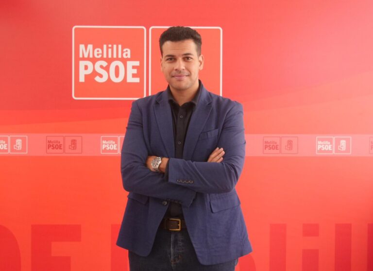 Hombre posando con brazos cruzados frente a un fondo rojo del PSOE en Melilla