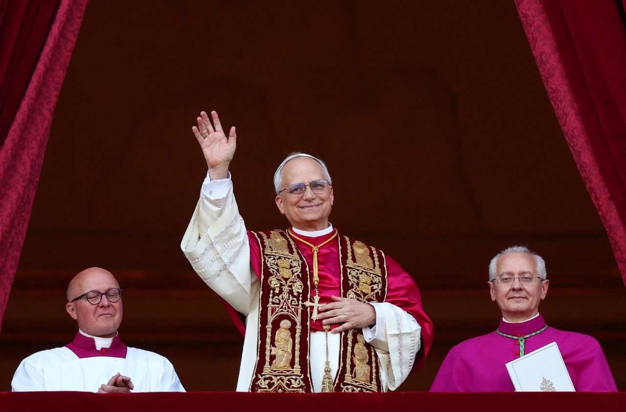 Papa XIV saludando desde el balcón con dos asistentes a su lado