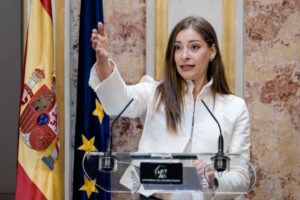 Mujer hablando en un podio con banderas de España y Europa detrás