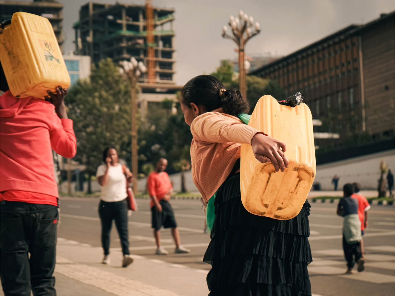 Fotografía de personas caminando con bidones amarillos en una calle