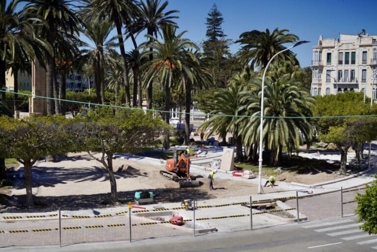 Construction work in a palm-tree park next to a street; an orange excavator and workers at the site.
