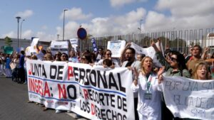 Group of protesters, including people in white coats, holding a large banner that reads 'JUNTA DE PERSONAL INGESA: NO A…' outside a fence.