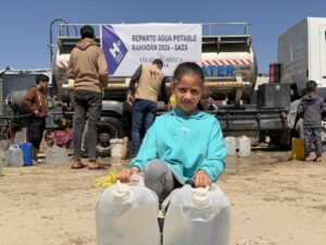 Niña sosteniendo botellas de agua en un reparto en Gaza