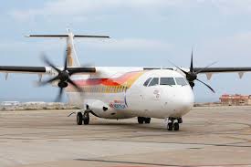 Twin-engine propeller airplane with rainbow stripe livery parked on an airport tarmac.