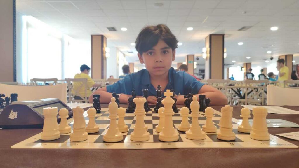 Niño jugando ajedrez en un torneo con piezas blancas y negras