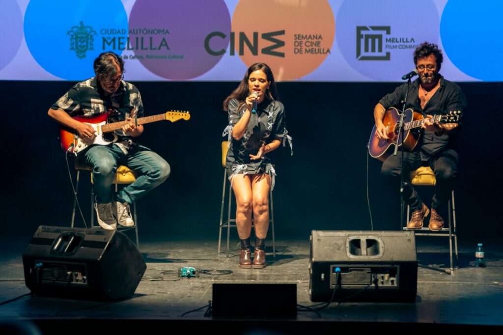 Actuación musical en la Semana de Cine de Melilla con tres artistas en el escenario.