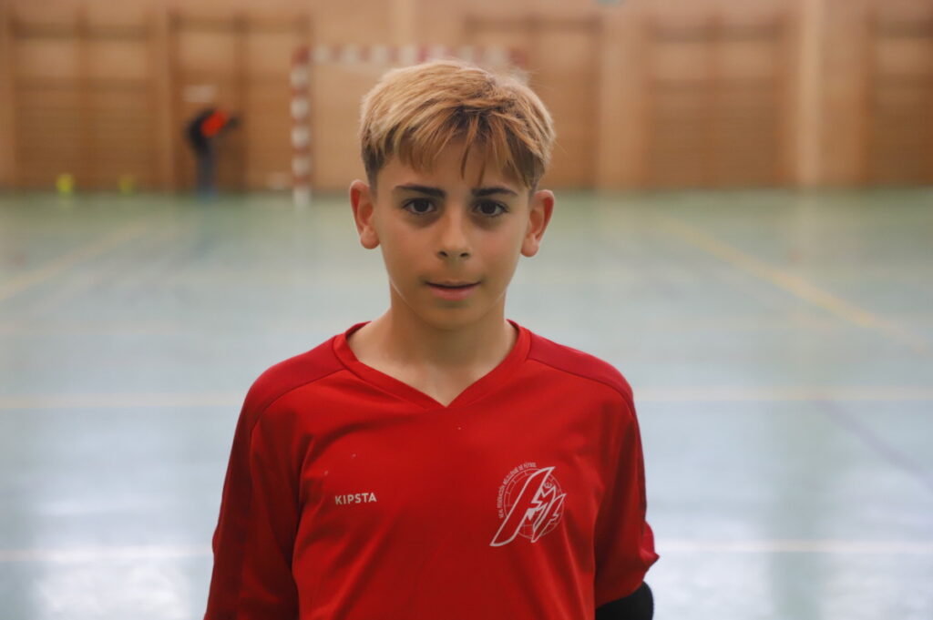 Boy in a red sports jersey facing the camera in an indoor gym.