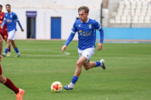Jugador de la U.D. Melilla corriendo con el balón en un partido de fútbol