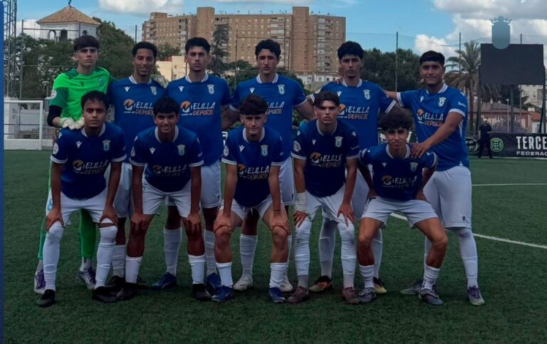 Youth soccer team posing for a group photo on a green turf field, blue jerseys and white shorts, near goalposts.