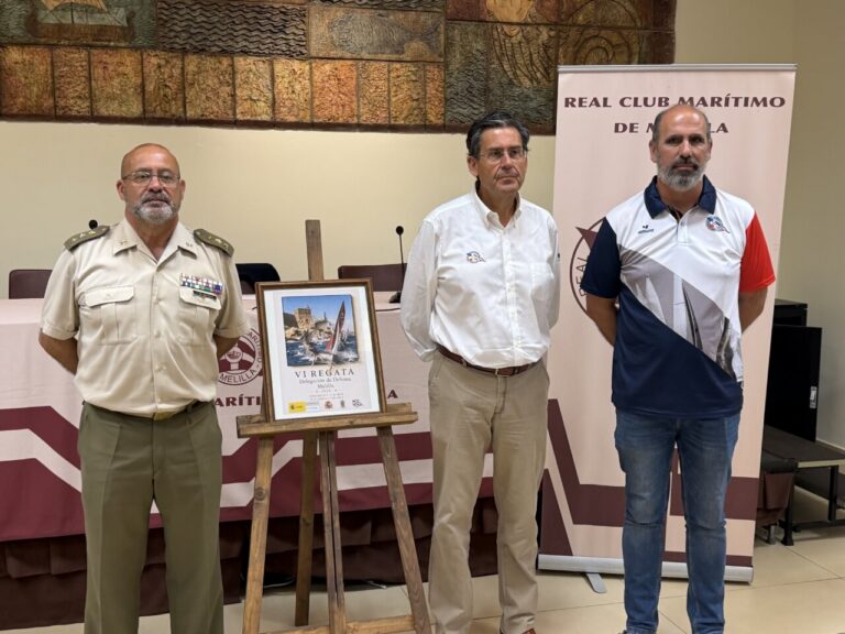 Tres hombres posando junto a un cartel de la VI Regata de Defensa en Melilla