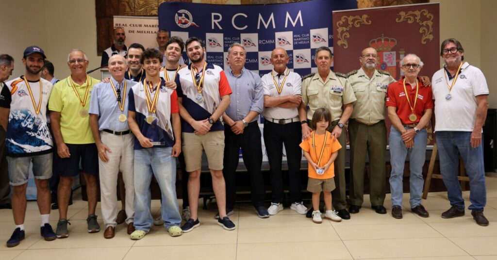 Group of men and a young girl posing with medals at an RCMM awards ceremony; backdrop features RCMM banners and logos.