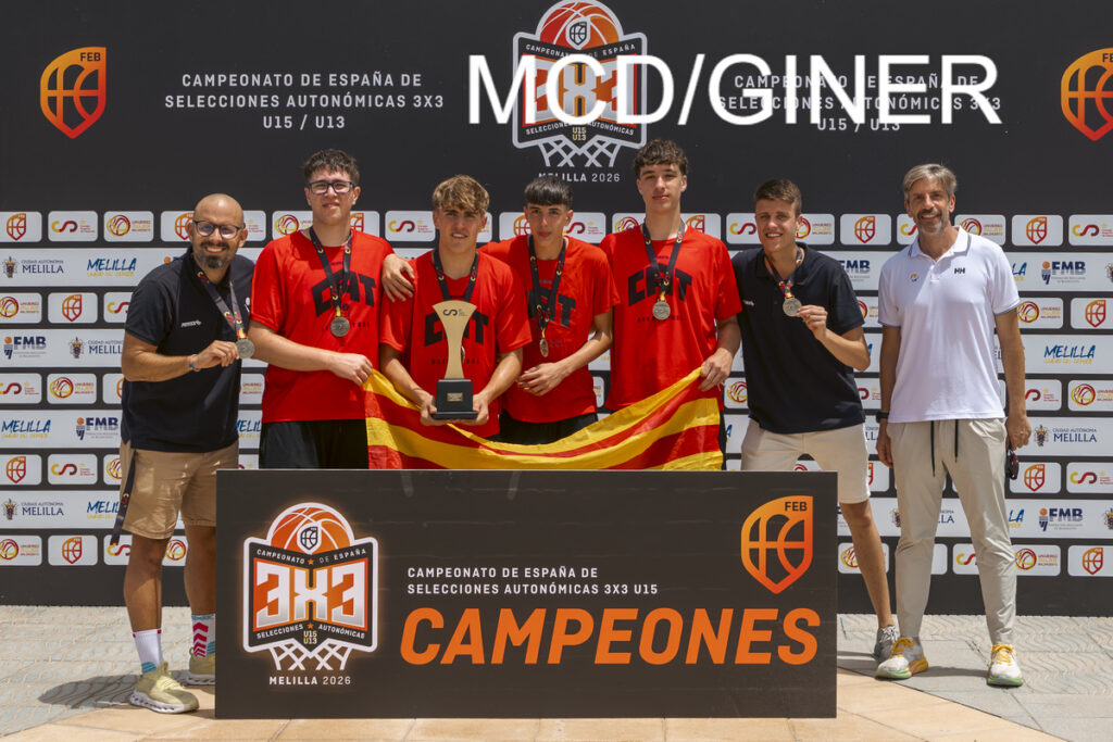 Youth basketball team posing with medals and a trophy, holding a Spanish flag under a 'CAMPEONES' banner after winning Spain 3x3 championships (U15/U13).