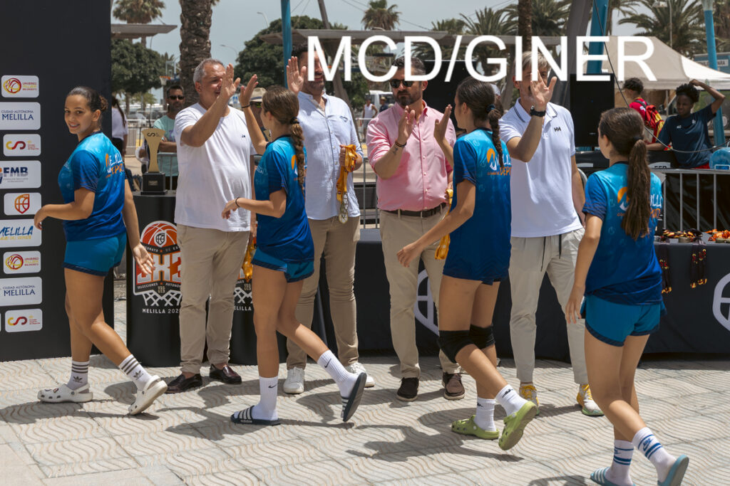 Group of young female basketball players in blue uniforms give high fives to adults at an outdoor awards ceremony.