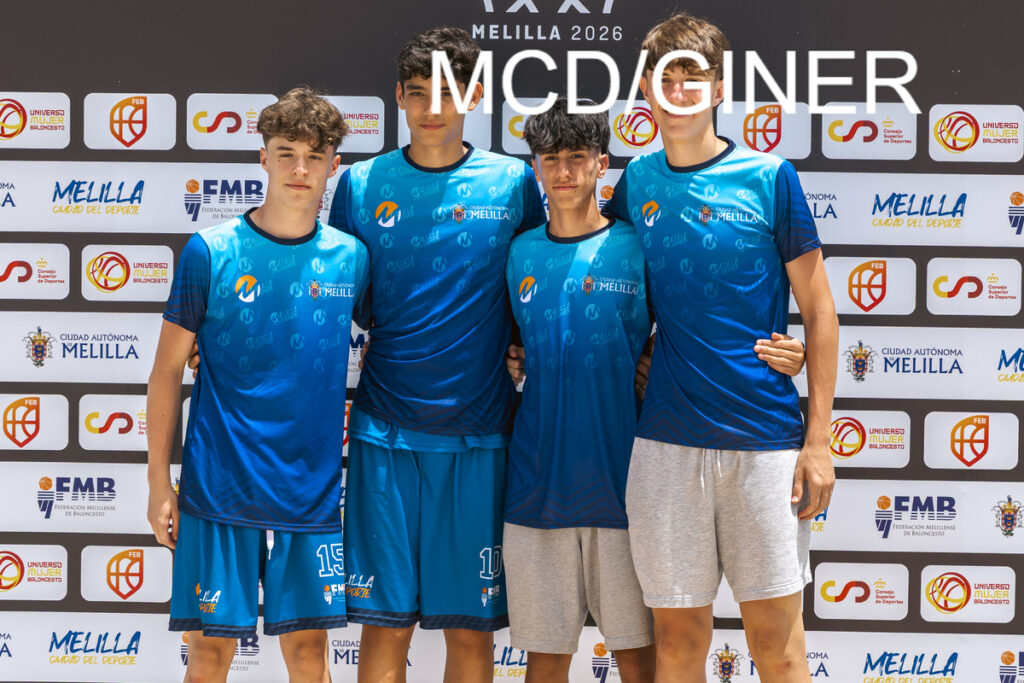 Four young basketball players in blue uniforms pose together in front of a sponsor backdrop at a sports event.