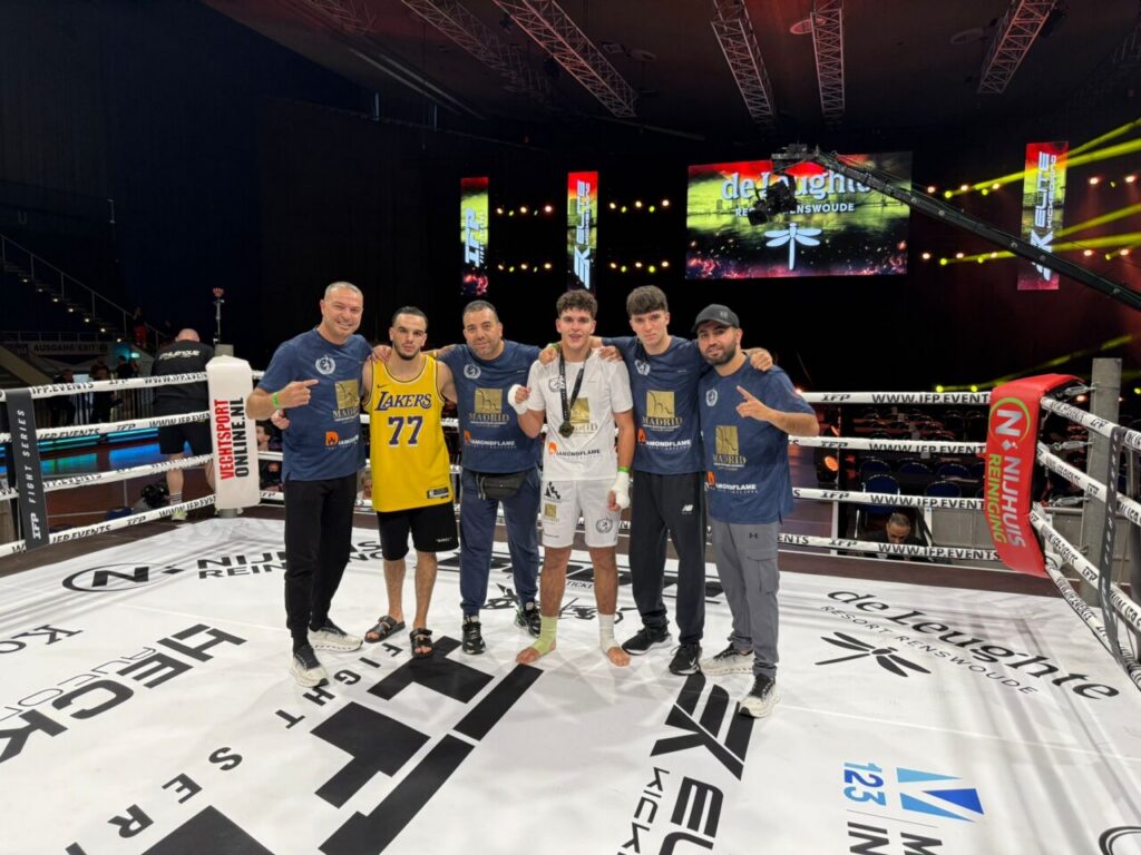 Group of six men posing in a boxing ring, two wearing fight shorts (one in yellow Lakers jersey) with coaches and teammates after a match.