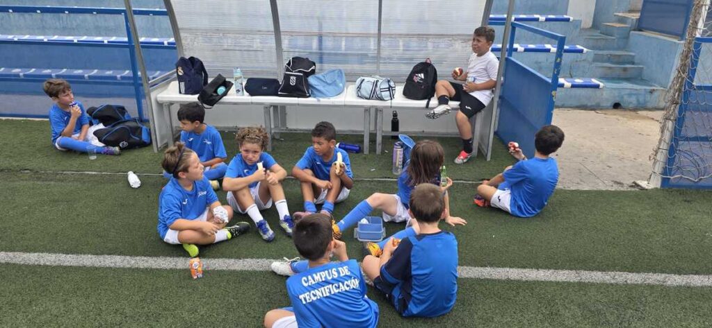 Niños en un campus de tecnificación de fútbol descansando en el campo