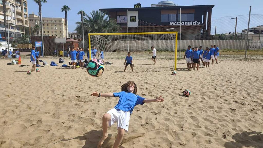 Niños jugando al fútbol en la playa con un balón colorido