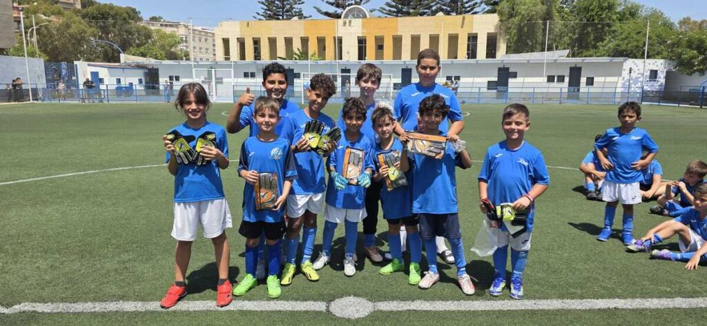 Grupo de niños en el campo de fútbol con camisetas azules sosteniendo guantes