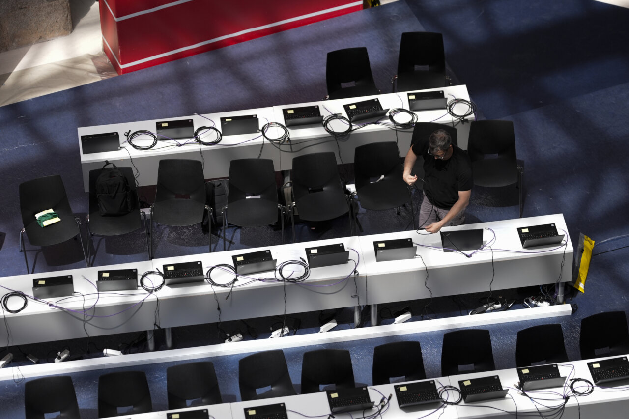 Overhead view of a computer lab with multiple desks, laptops, cables, and chairs, as a technician wires equipment.