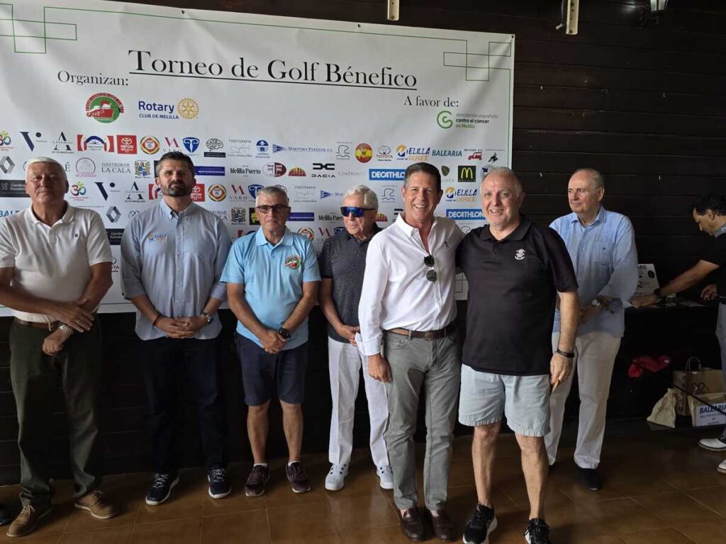 Group of eight men posing for a photo indoors in front of a banner that reads 'Torneo de Golf Benéfico'; sponsor logos are visible on the banner.